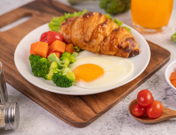 Breakfast consisting of bread, fried eggs, broccoli, carrots, tomatoes and lettuce on a white plate