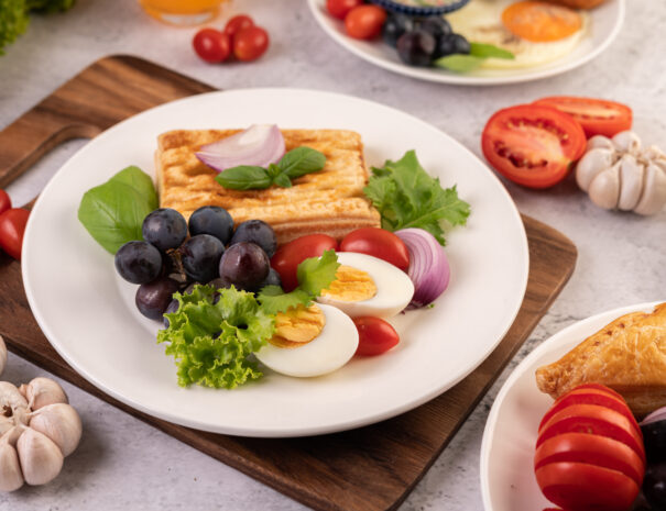 Breakfast consists of bread, boiled eggs, black grape salad dressing, tomatoes, and sliced ​​onions.